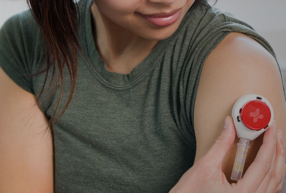 Person holding an upper-arm blood collection device against their arm.